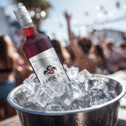 „Flasche FICKEN Likör im Eiskübel mit Eiswürfeln, draußen bei Sonnenschein, im Hintergrund feiernde Menschen